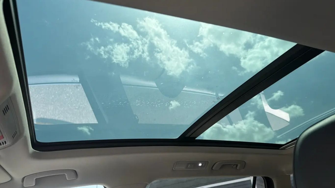 Car interior with a panoramic sunroof showing a blue sky and clouds above