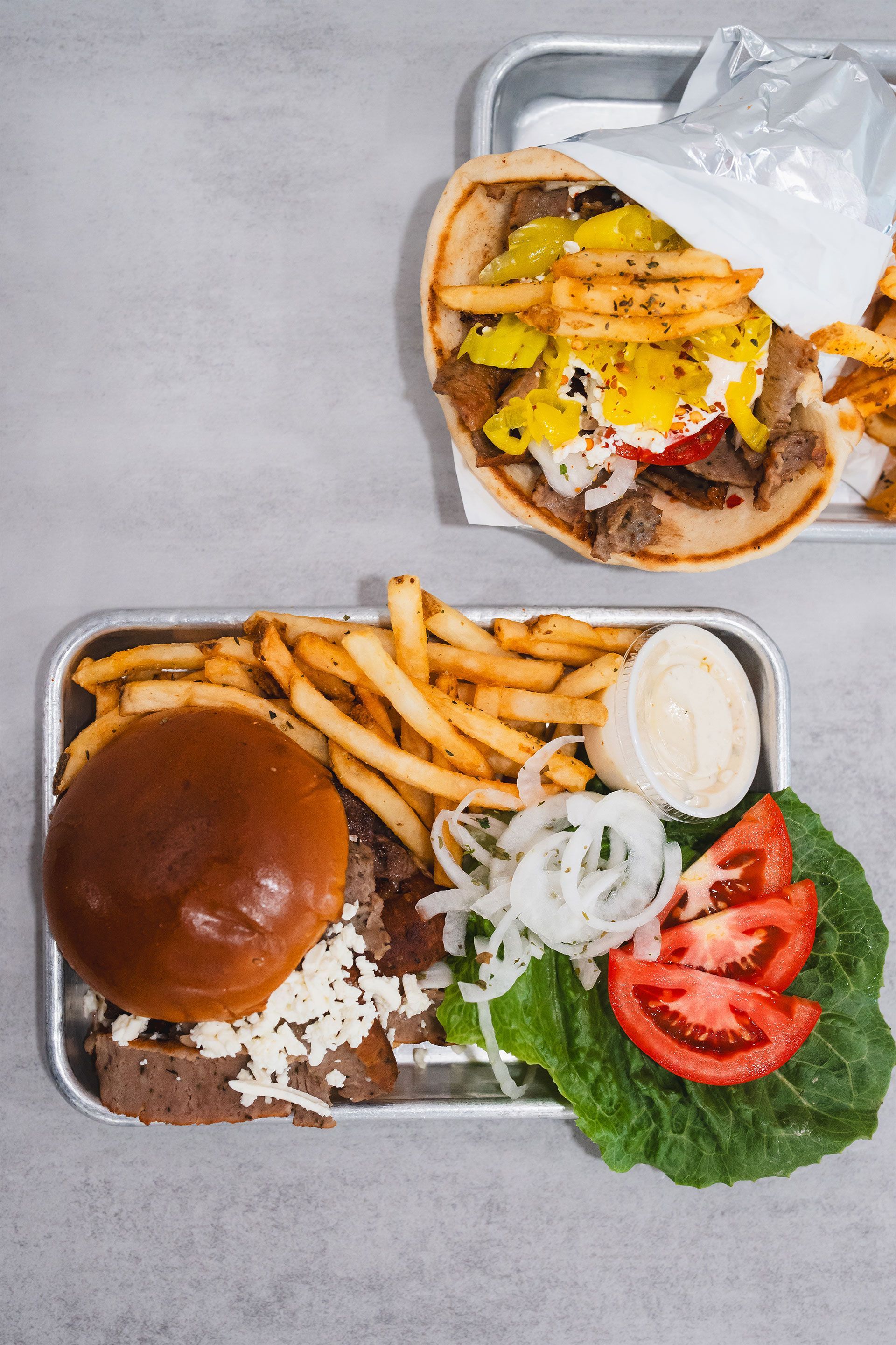 A gyro sandwich and french fries on a metal tray on a table