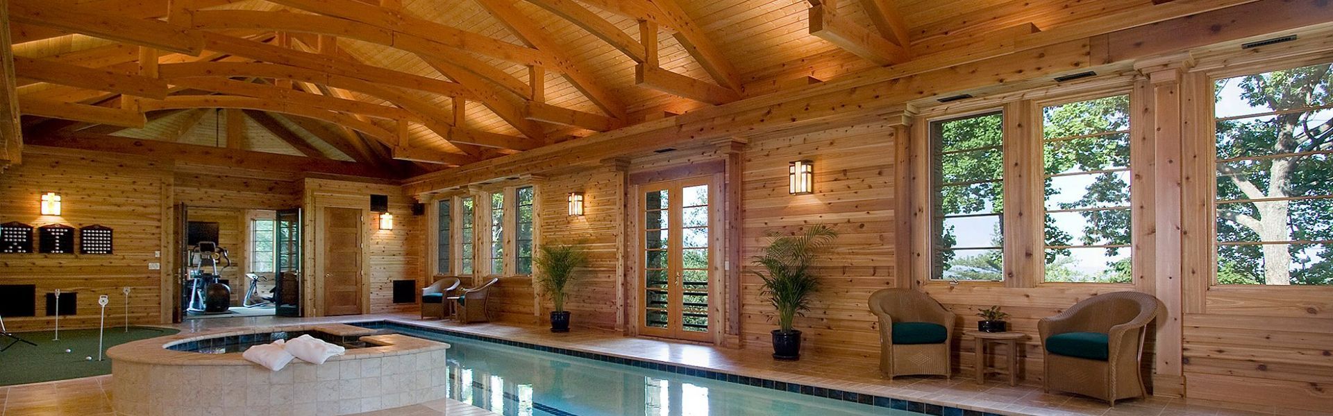 Indoor swimming pool with wooden walls and ceiling, large windows, and a jacuzzi area.