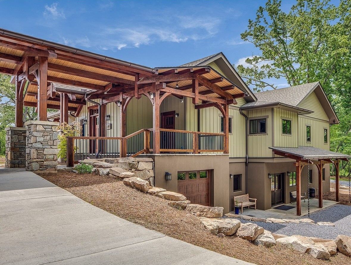 Wooden cabin with porch and stone accents. Driveway leads up to the house.