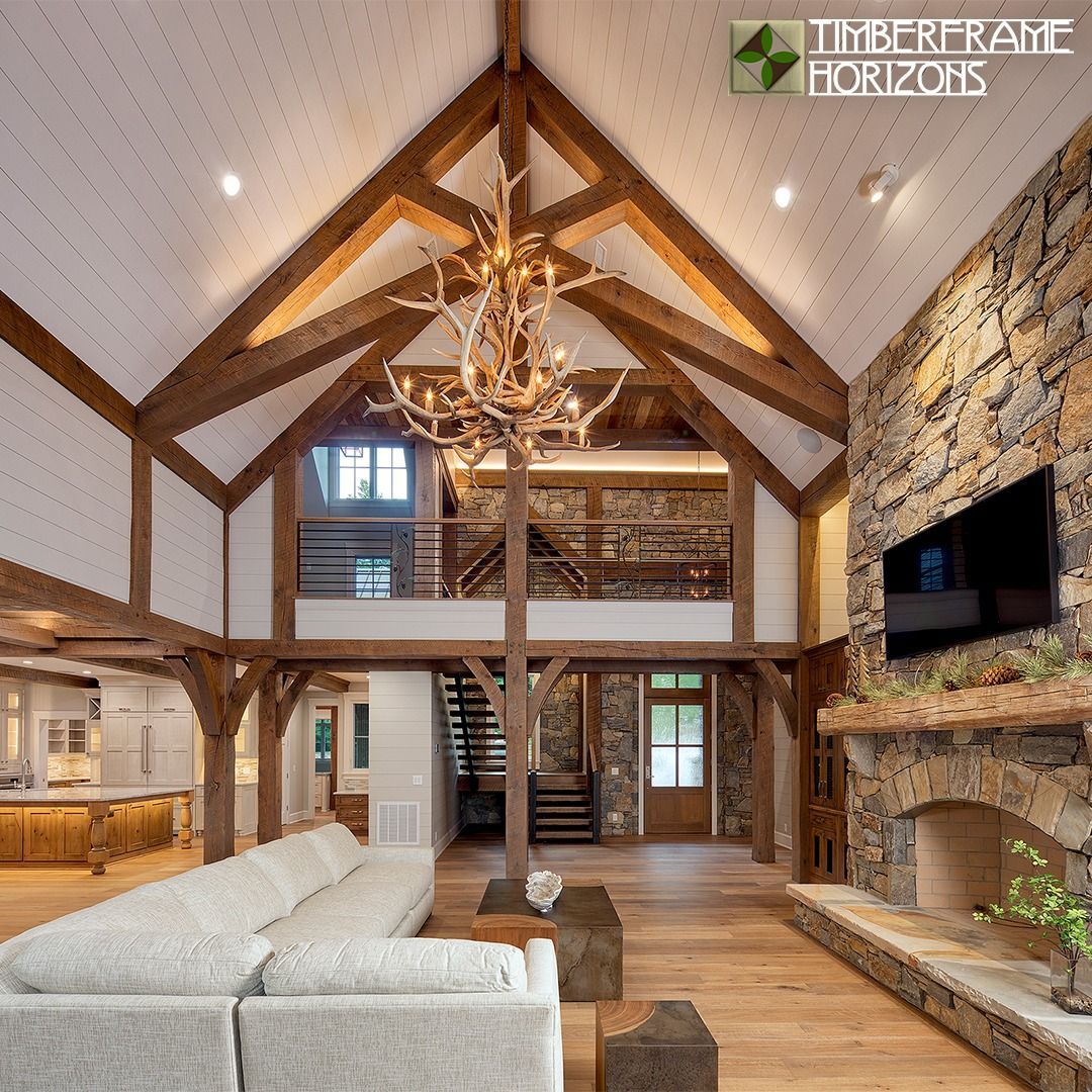 Living room with timber frame beams, stone fireplace, and chandelier.