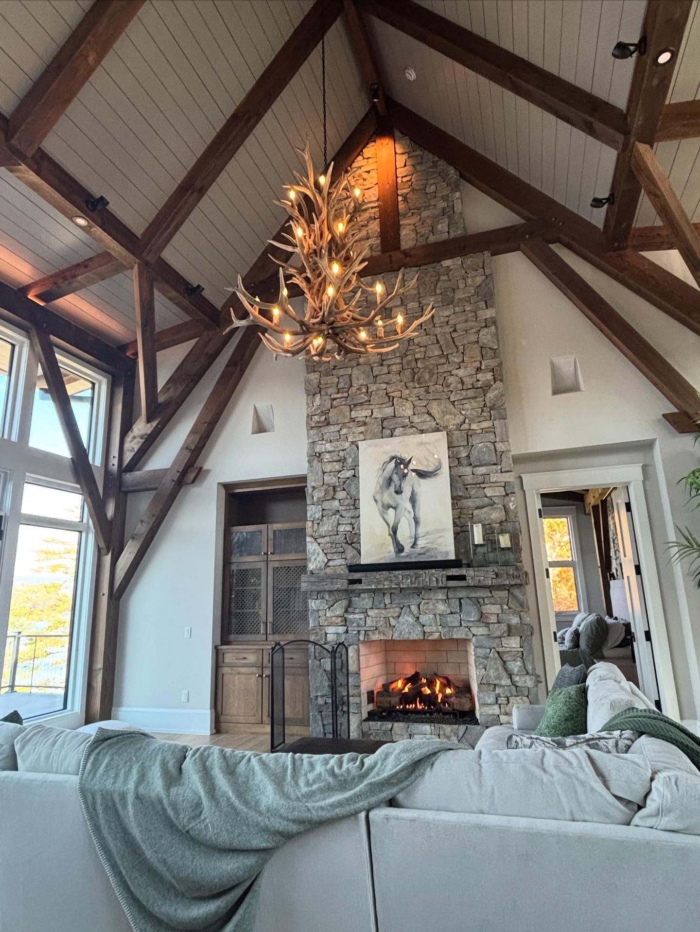Living room with stone fireplace, antler chandelier, and wood beams.