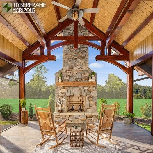 Screened-in porch with fireplace, timber frame, rocking chairs, and view of a green field.