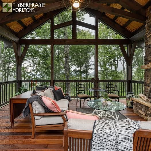 Wooden porch with seating, fireplace, and glass windows overlooking trees.