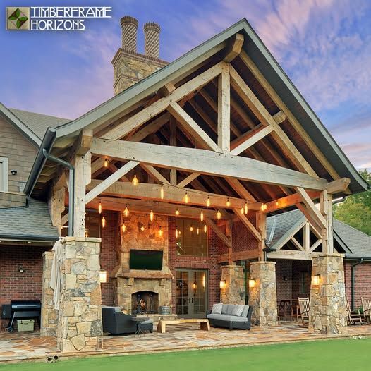 Timber-framed covered patio with fireplace, stone pillars, hanging lights, and seating area.