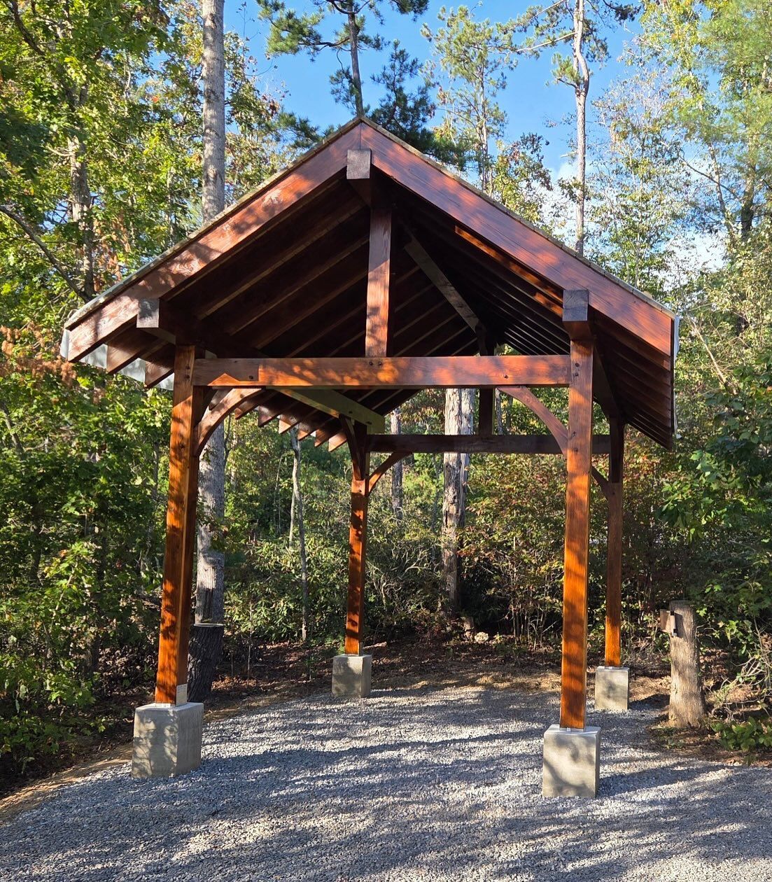 Wooden shelter in a forest, brown roof and supports, gray gravel ground.