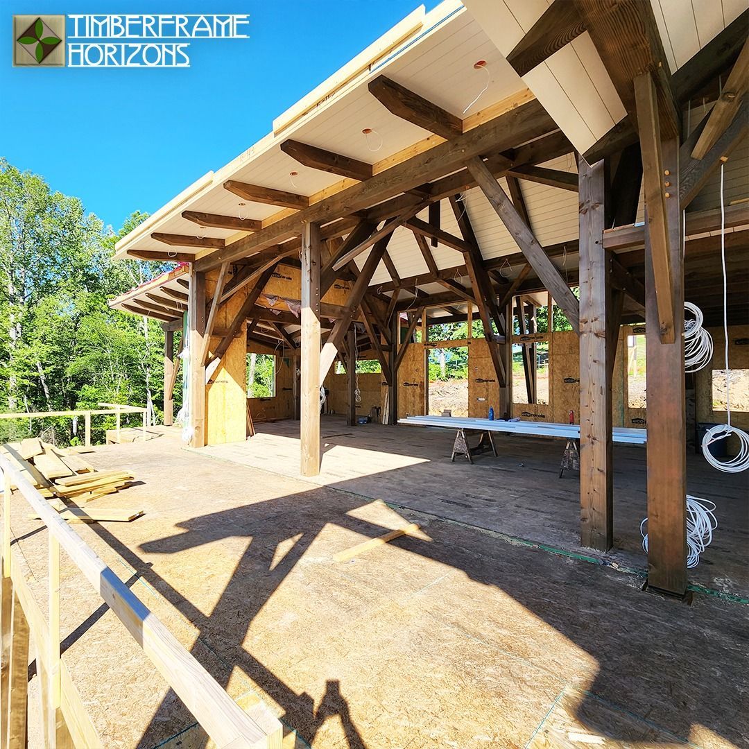 Timber-framed outdoor pavilion with open sides and light roof, built on a gravel base. Sunny day.