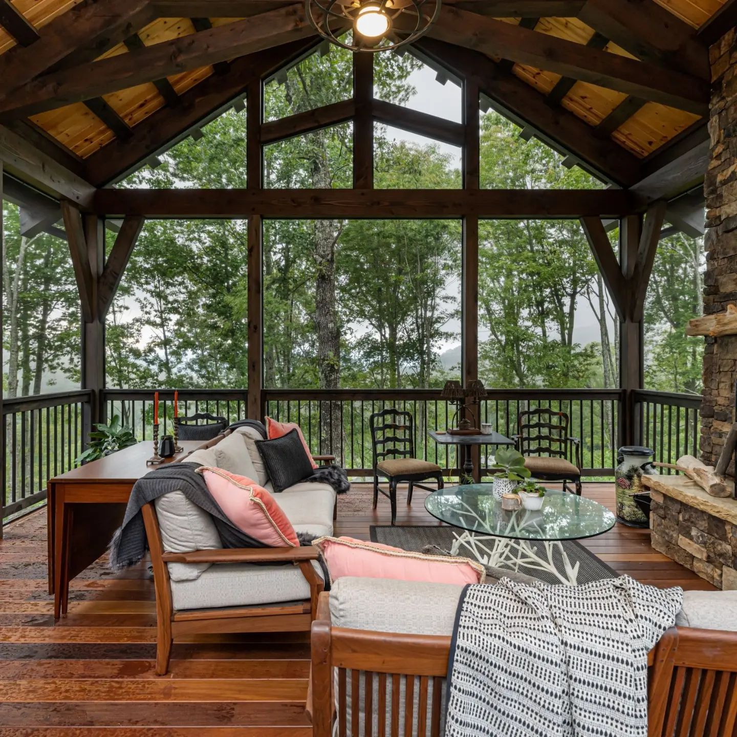 Screened-in porch with wood furniture, stone fireplace, and view of trees.