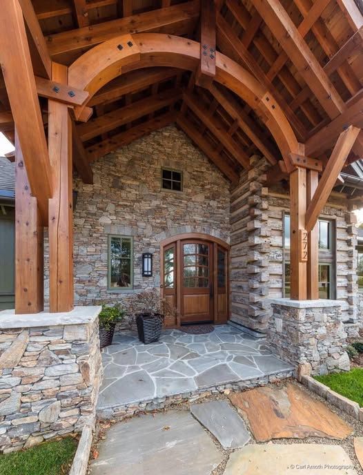 Stone and timber entry of a house with a curved wooden beam, arched door, and flagstone path.