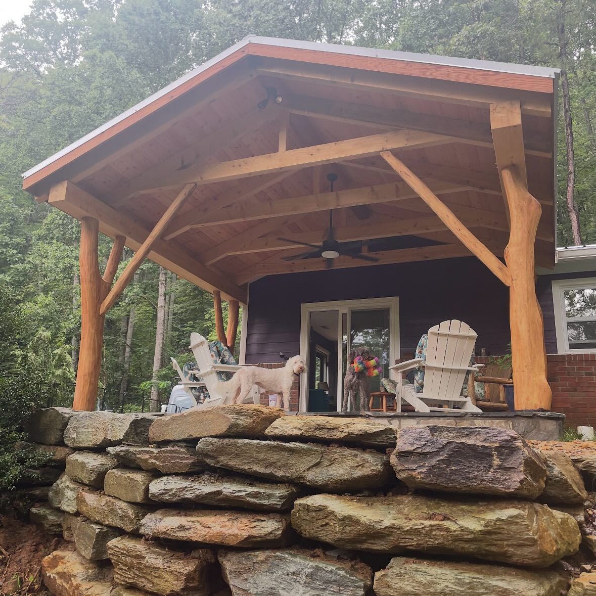 Rustic porch with stone wall, wooden beams, purple house, and dog.