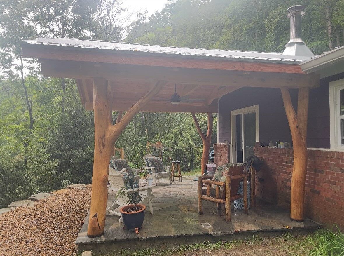 Porch with wooden beams and metal roof, overlooking a wooded area. Furniture on the porch.