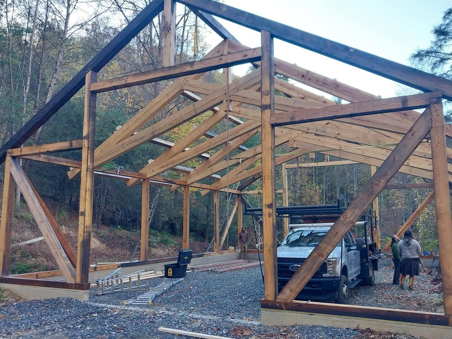 Wooden frame of a barn under construction with a truck and people nearby.