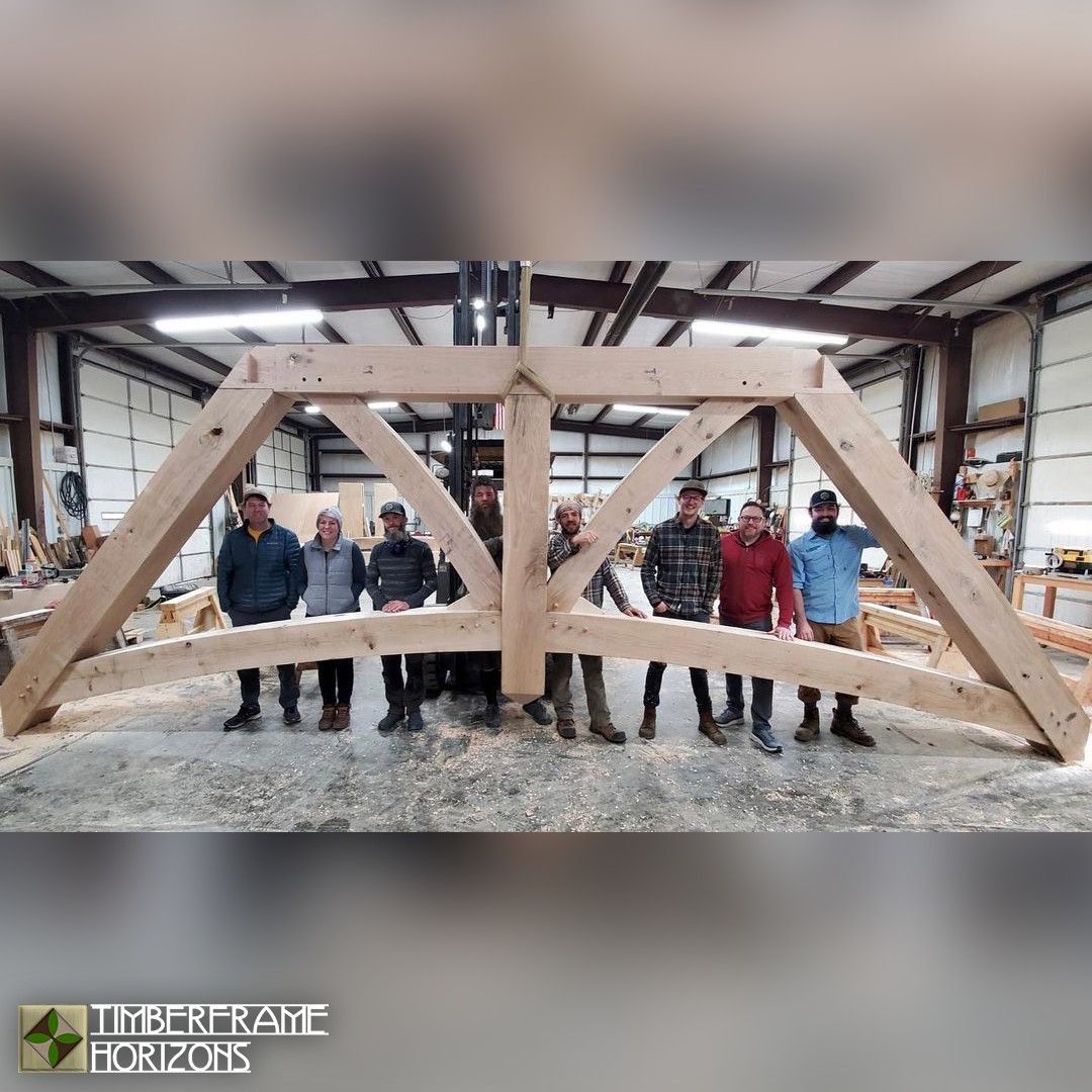 Group of people pose with a large wooden arch in a workshop.