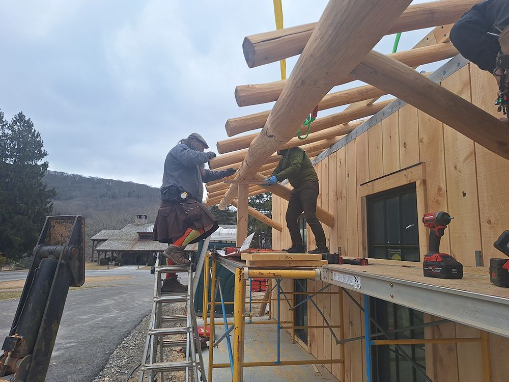 Construction workers installing wooden beams on a building's roof. Scaffold and a crane are present.