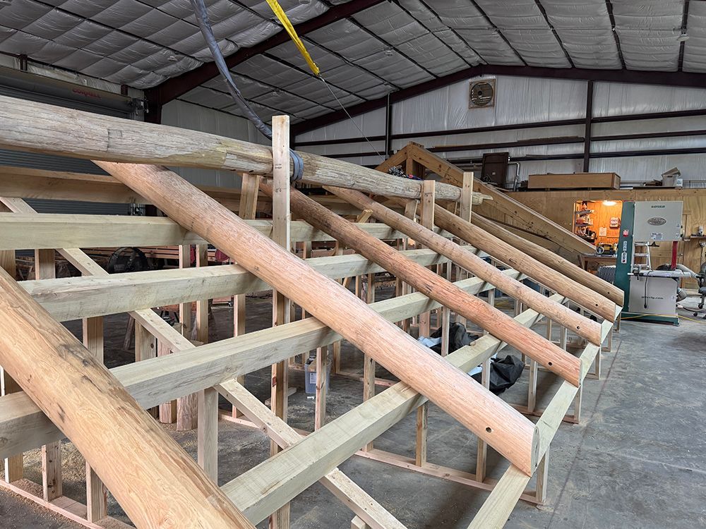 Wooden roof frame under construction inside a workshop; beams and posts are visible.