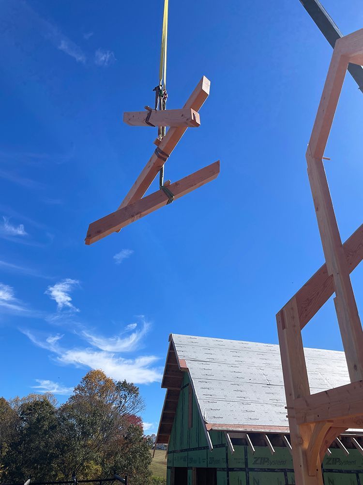 A crane lifting a wooden beam into place on a building frame, blue sky in the background.