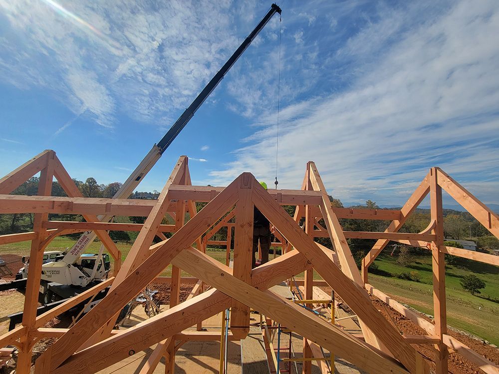 Construction workers assembling a wooden roof frame with a crane on a sunny day.