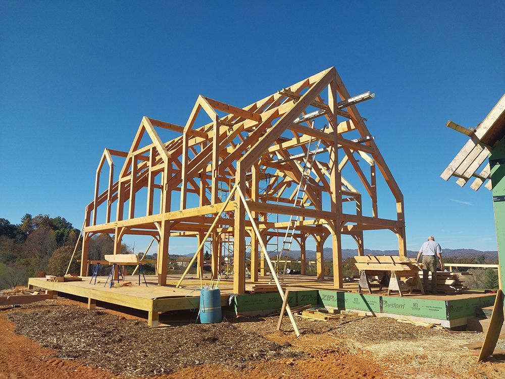 Wooden timber frame house under construction against a blue sky, with a person working.