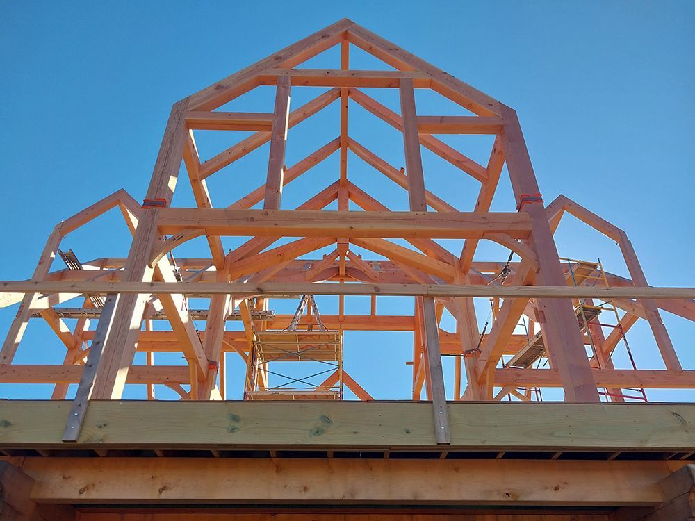 Wooden framework of a building under construction against a clear blue sky.