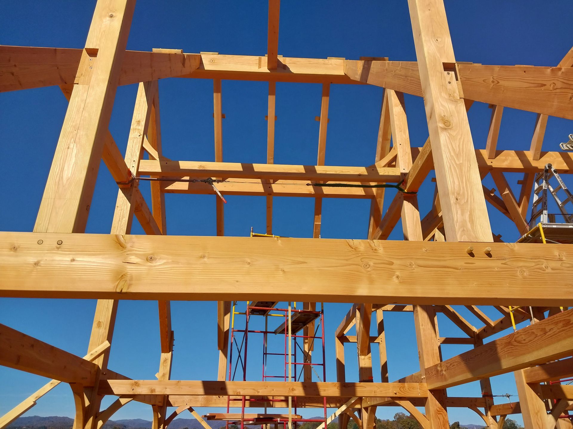 Wooden timber frame construction against a clear blue sky; scaffolding visible.
