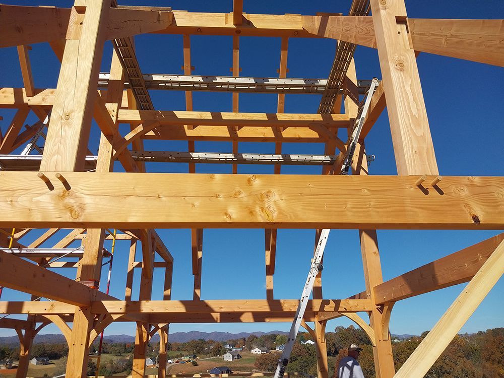 Wooden timber frame construction against a blue sky, with a person visible below.