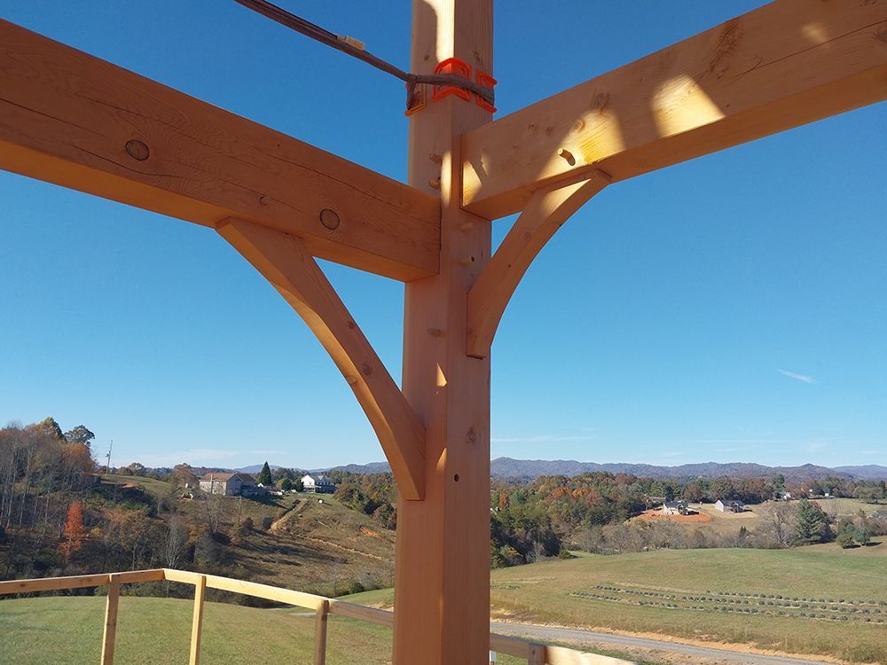 Wooden timber frame construction with a view of a rural landscape under a blue sky.