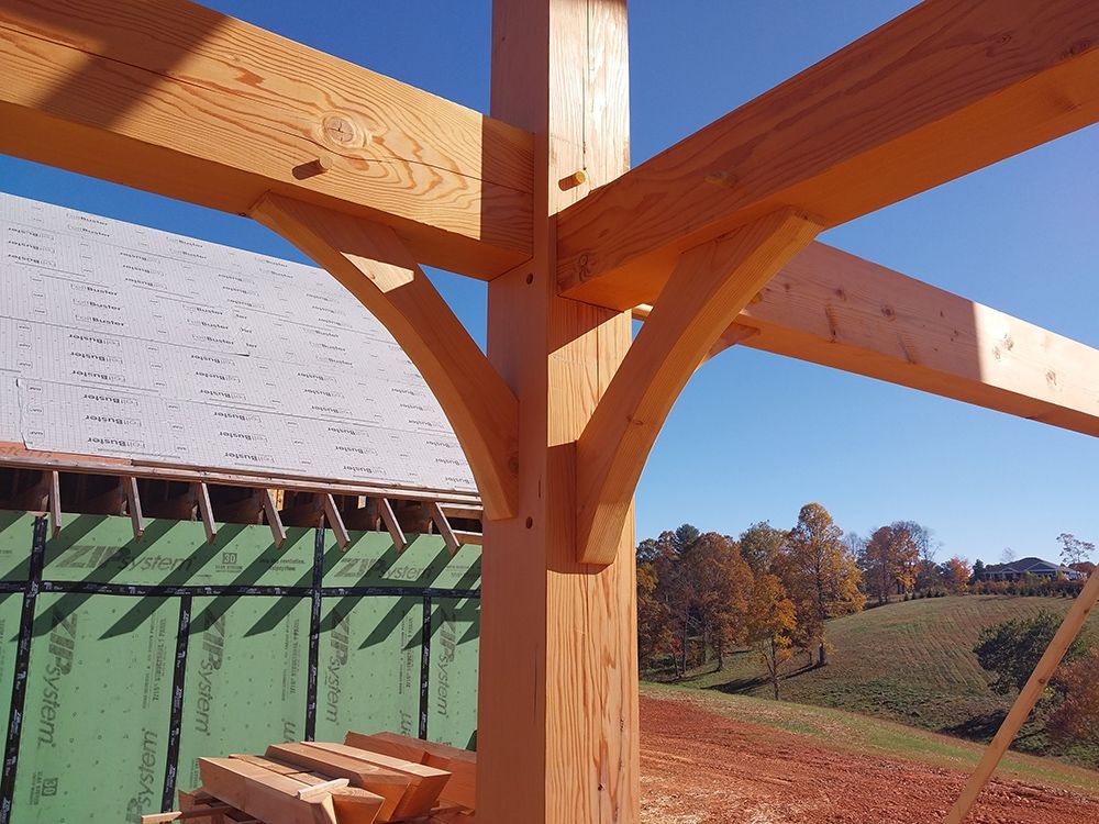 Wooden timber frame construction with curved braces, blue sky backdrop.