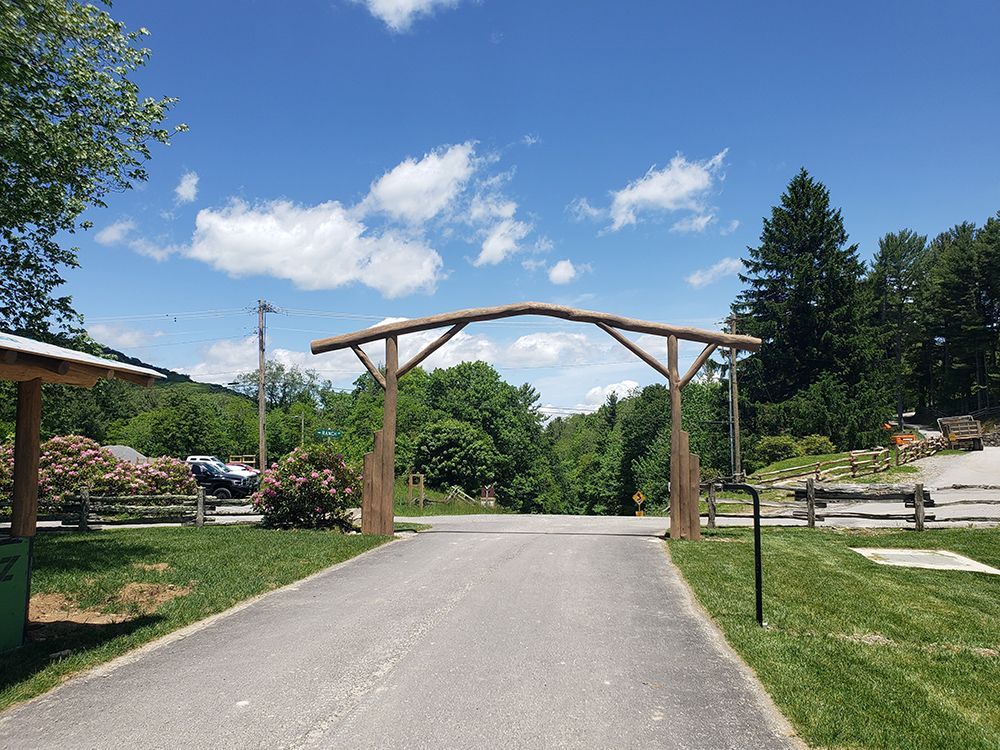 Wooden archway over paved road leading into a green landscape under a blue sky.