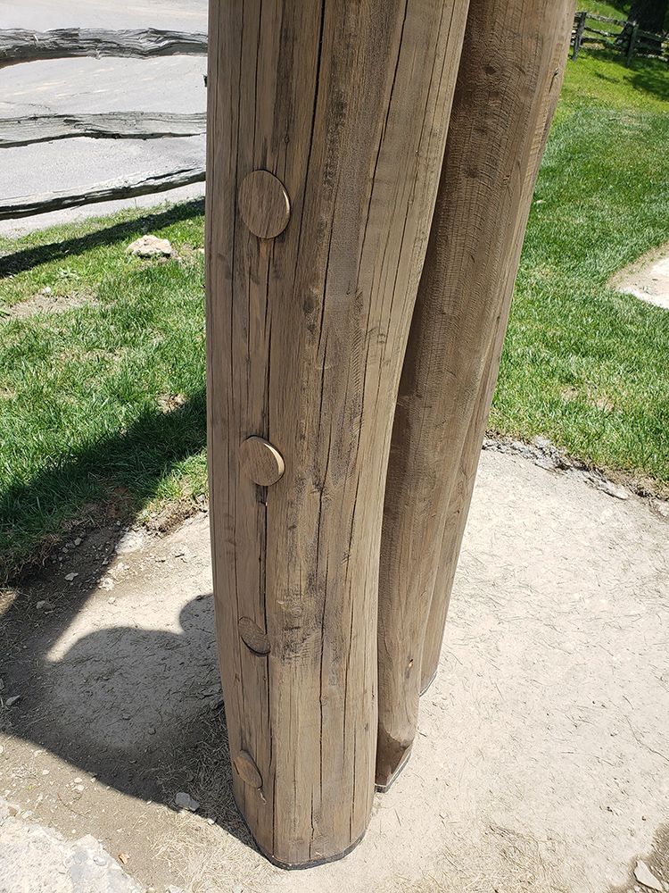 Close-up of weathered wooden posts secured to a concrete base with visible fasteners. Green grass in the background.