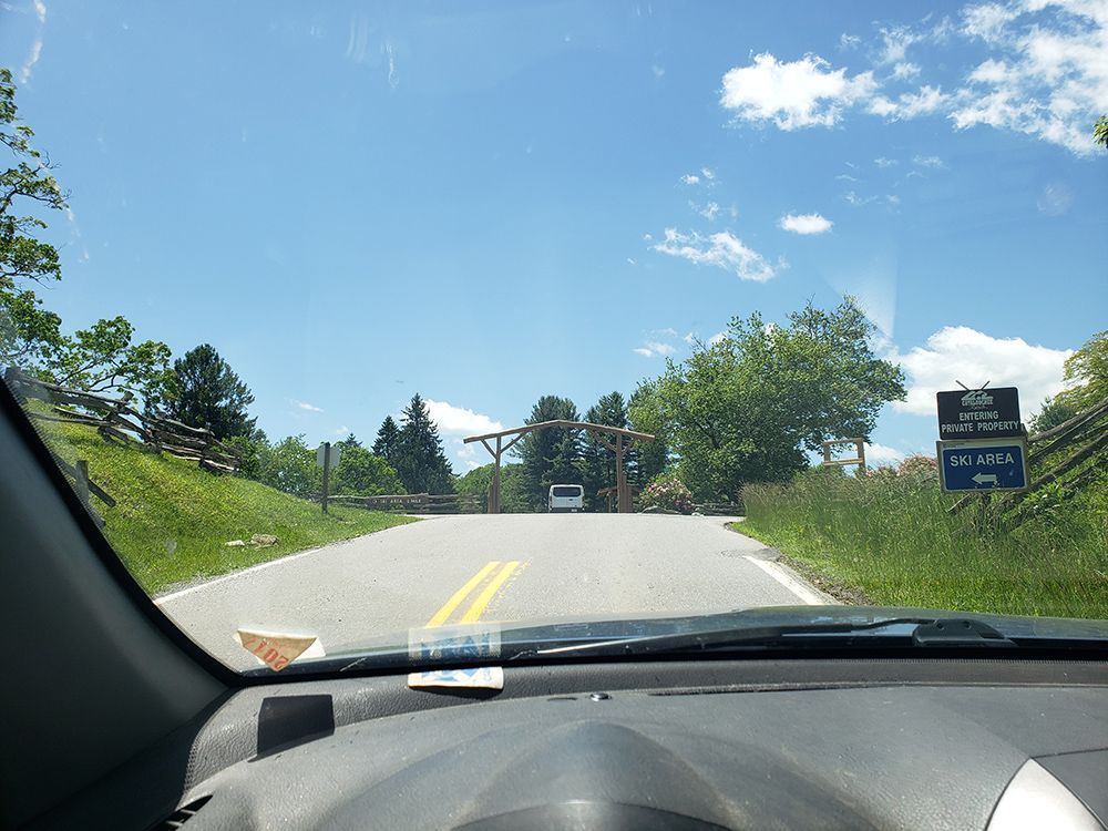 View from inside a car driving towards a park entrance on a sunny day.