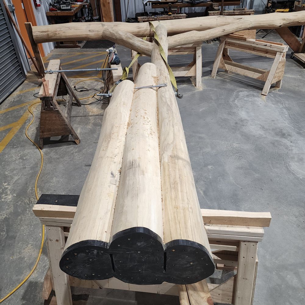Three light-colored logs with black ends bundled together on a wooden frame, workshop setting.