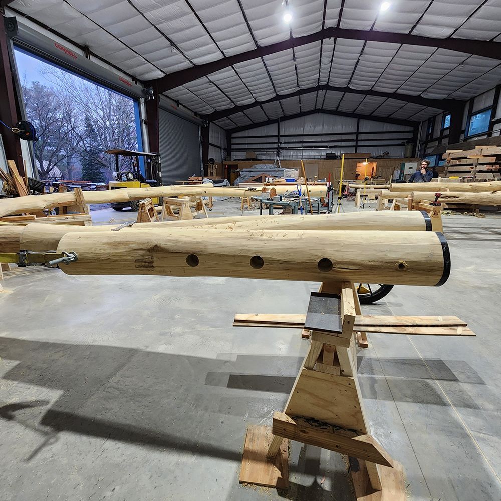 Logs with holes, supported on wooden sawhorses, inside a large workshop.