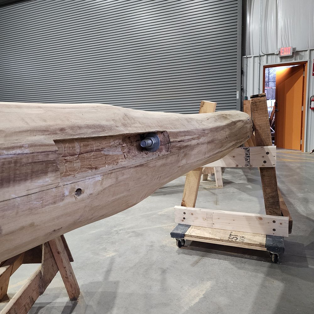 A large wooden beam with metal hardware is on saw horses in a workshop.