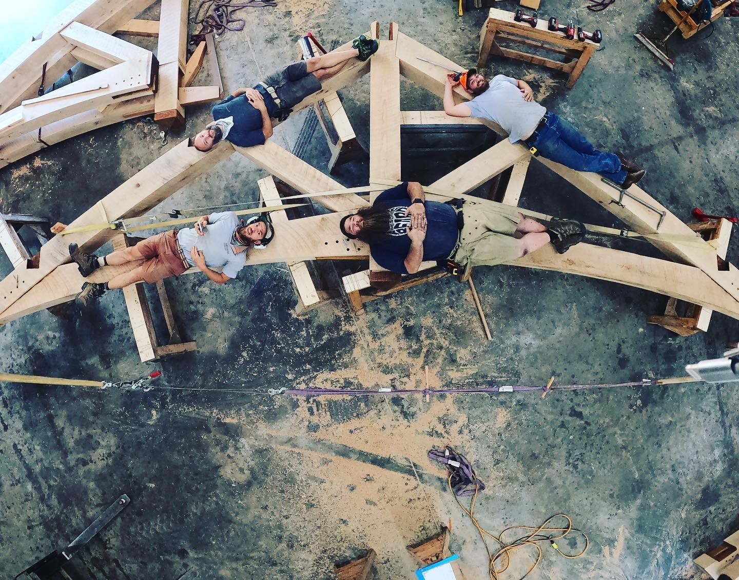 Five people resting on a large wooden structure. Overhead shot on a construction site.