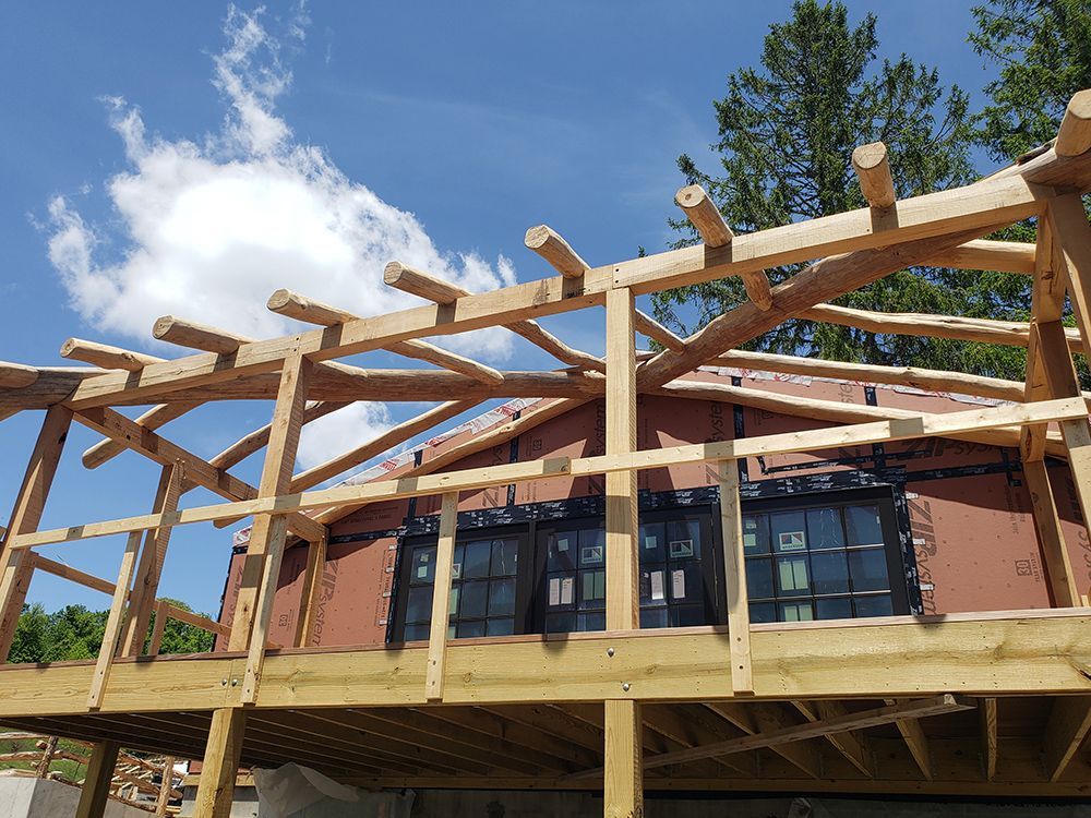 Wooden structure being built around dark framed windows on a deck, with a blue sky background.