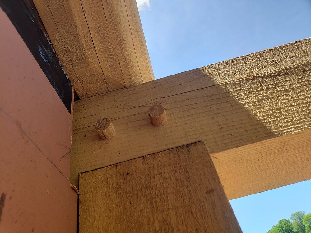 Wooden beams joined with pegs at a building's corner against a blue sky.