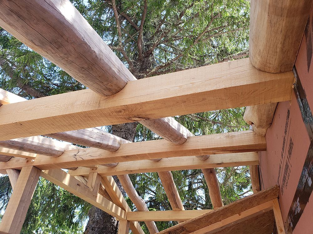 Wooden beams and rafters form a roof structure, with insulation and a tree visible in the background.