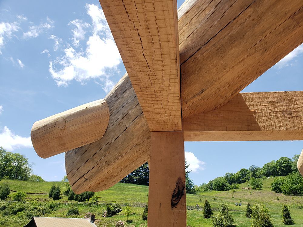 Wooden beams of a pergola frame against a blue sky, overlooking a green hillside.