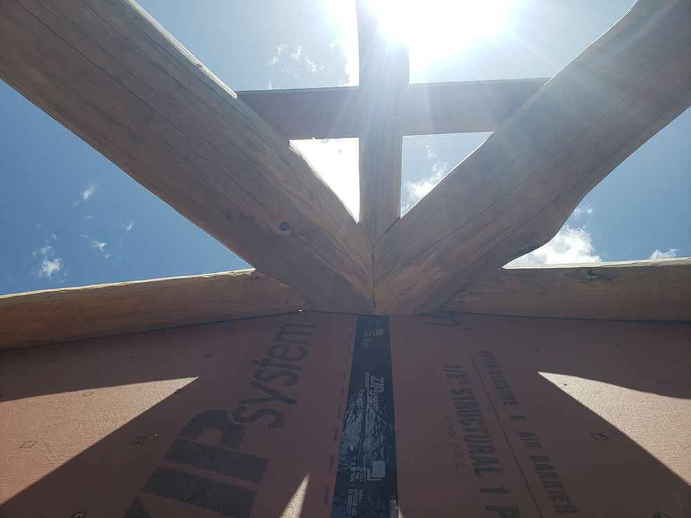 Wooden roof beams intersecting against a bright blue sky. Brown insulation is below.