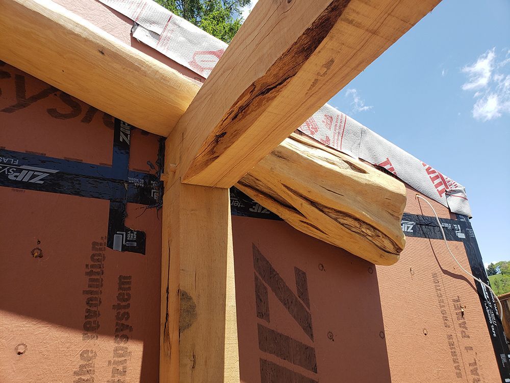 Wooden beams forming the frame of a structure; fastened to a brown wall with black tape; against a blue sky.