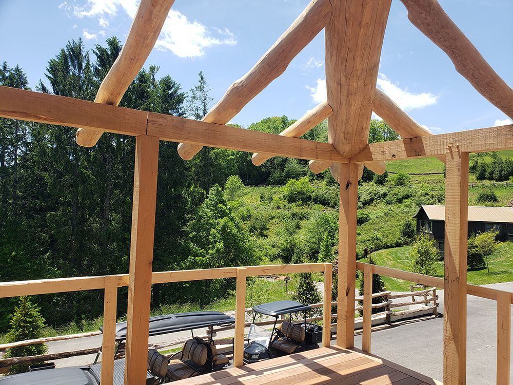 Wooden porch with log beams, golf carts, and a forested hillside on a sunny day.