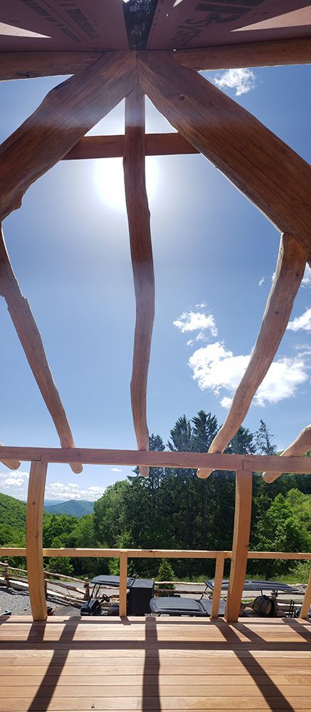 Wooden deck under blue sky through log cabin frame, sun shining above trees and distant mountains.