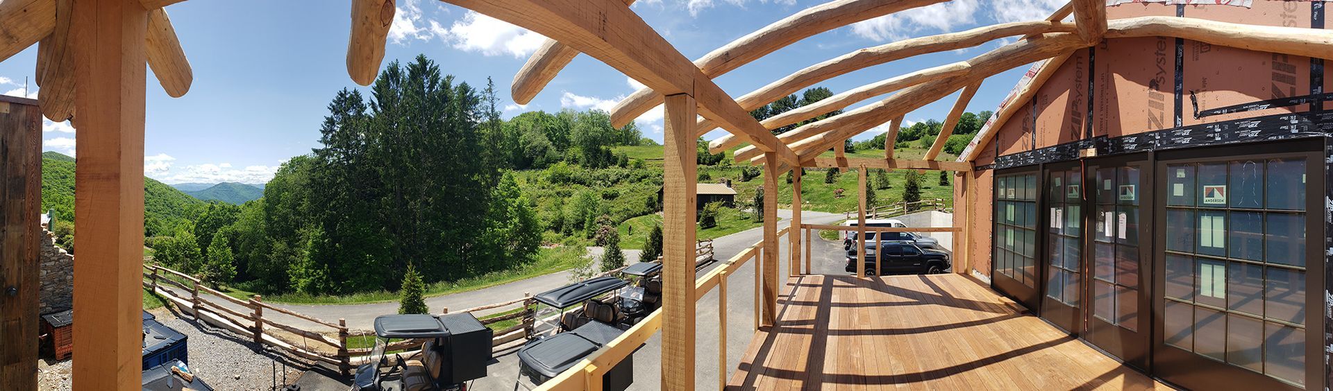 Wooden deck with curved roof, looking out at a green landscape and blue sky.