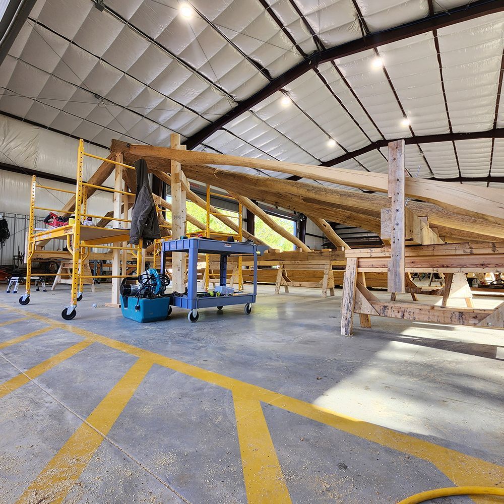 Wooden roof structure under construction inside a workshop, with scaffolding and tools.
