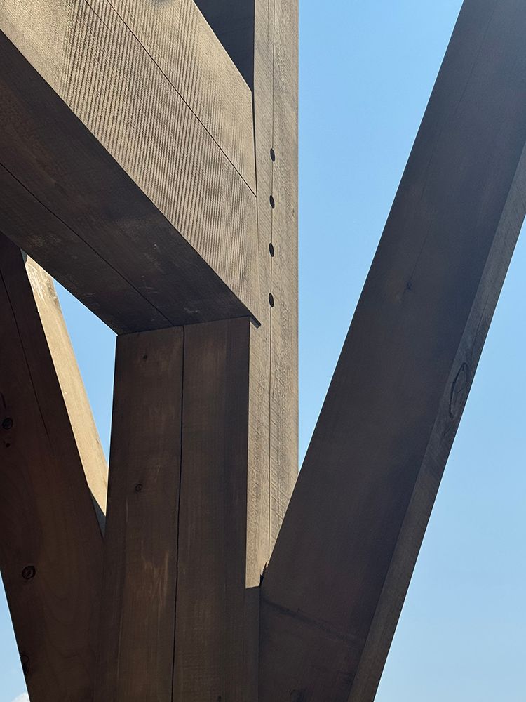 Dark wooden beams form an architectural structure against a bright blue sky.