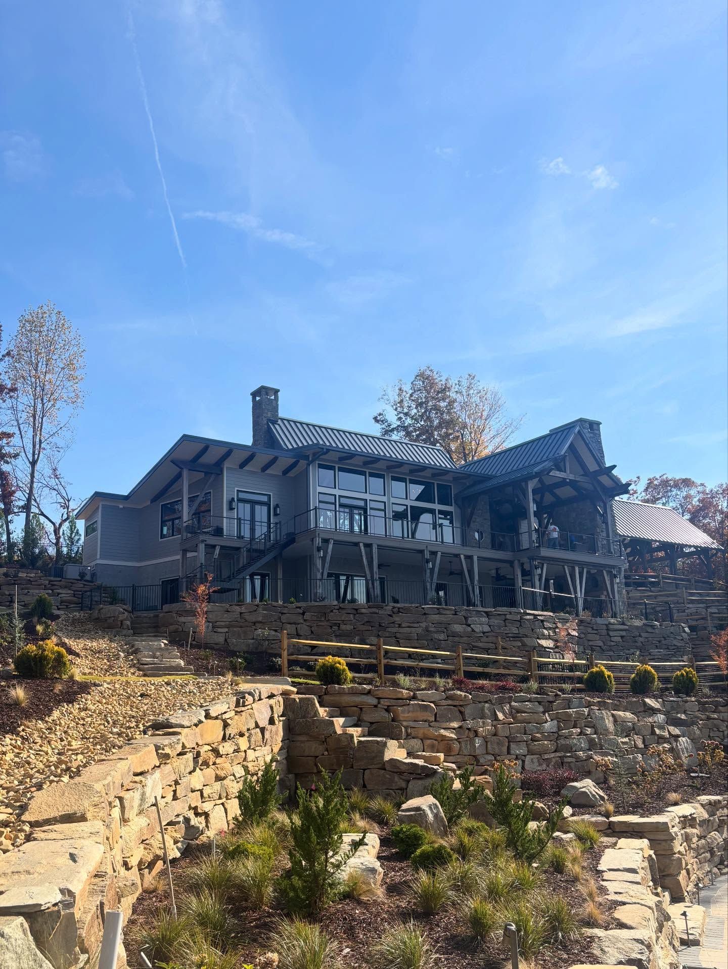 Large gray house with stone retaining walls, blue sky.