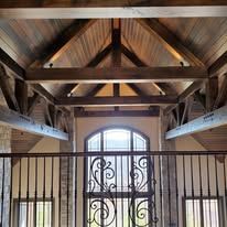 Wooden beams and trusses in an entryway, with a large arched window and wrought iron gate.