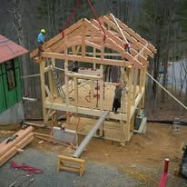 Wooden structure of a small building under construction; workers on roof. Outdoors.