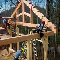Construction workers building a wooden structure outdoors. One worker is securing a beam.