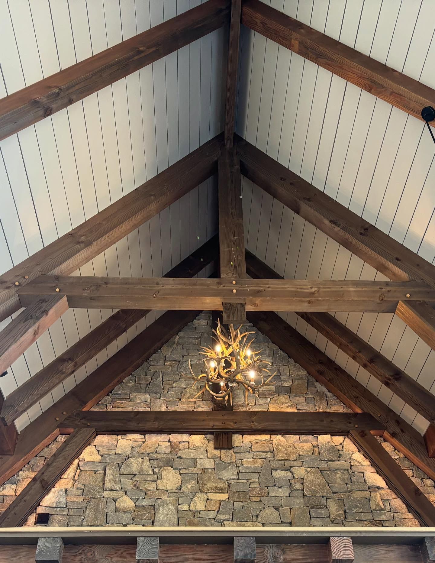 Wooden beams frame a vaulted ceiling with white panels. A stone wall and chandelier are below.